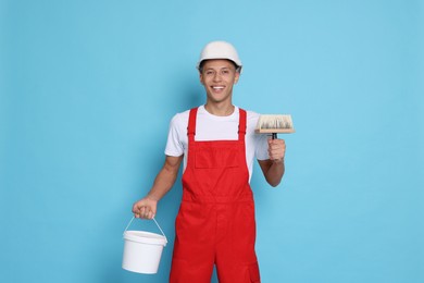 Photo of Portrait of young decorator with bucket and brush on light blue background