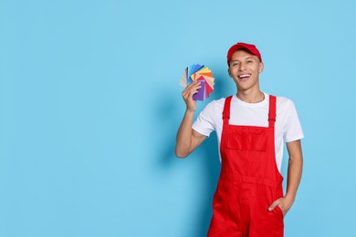 Photo of Portrait of young decorator with color palettes on light blue background, space for text