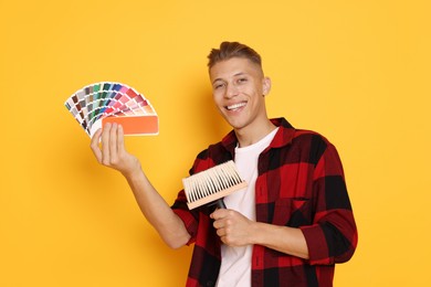 Photo of Portrait of young decorator with color palettes and brush on orange background