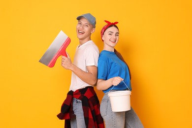 Photo of Professional decorator. Man and woman with different tools on orange background