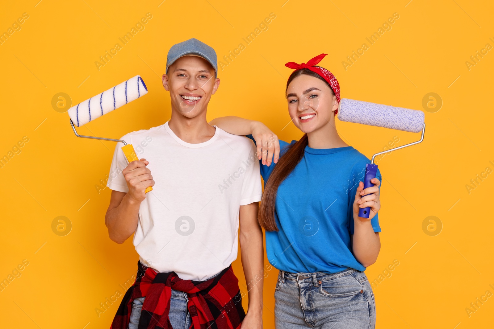 Photo of Professional decorator. Man and woman with paint rollers on orange background