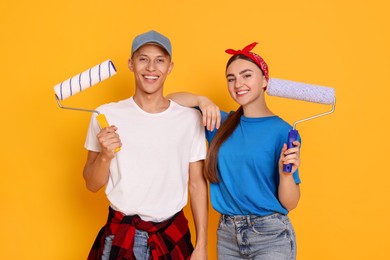 Photo of Professional decorator. Man and woman with paint rollers on orange background