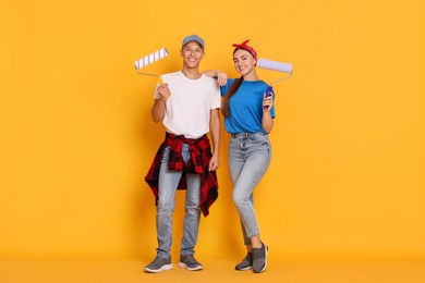 Photo of Professional decorator. Man and woman with paint rollers on orange background