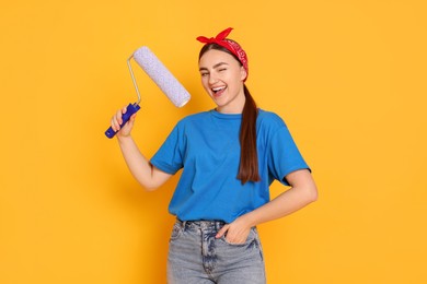 Photo of Portrait of young decorator with paint roller on orange background