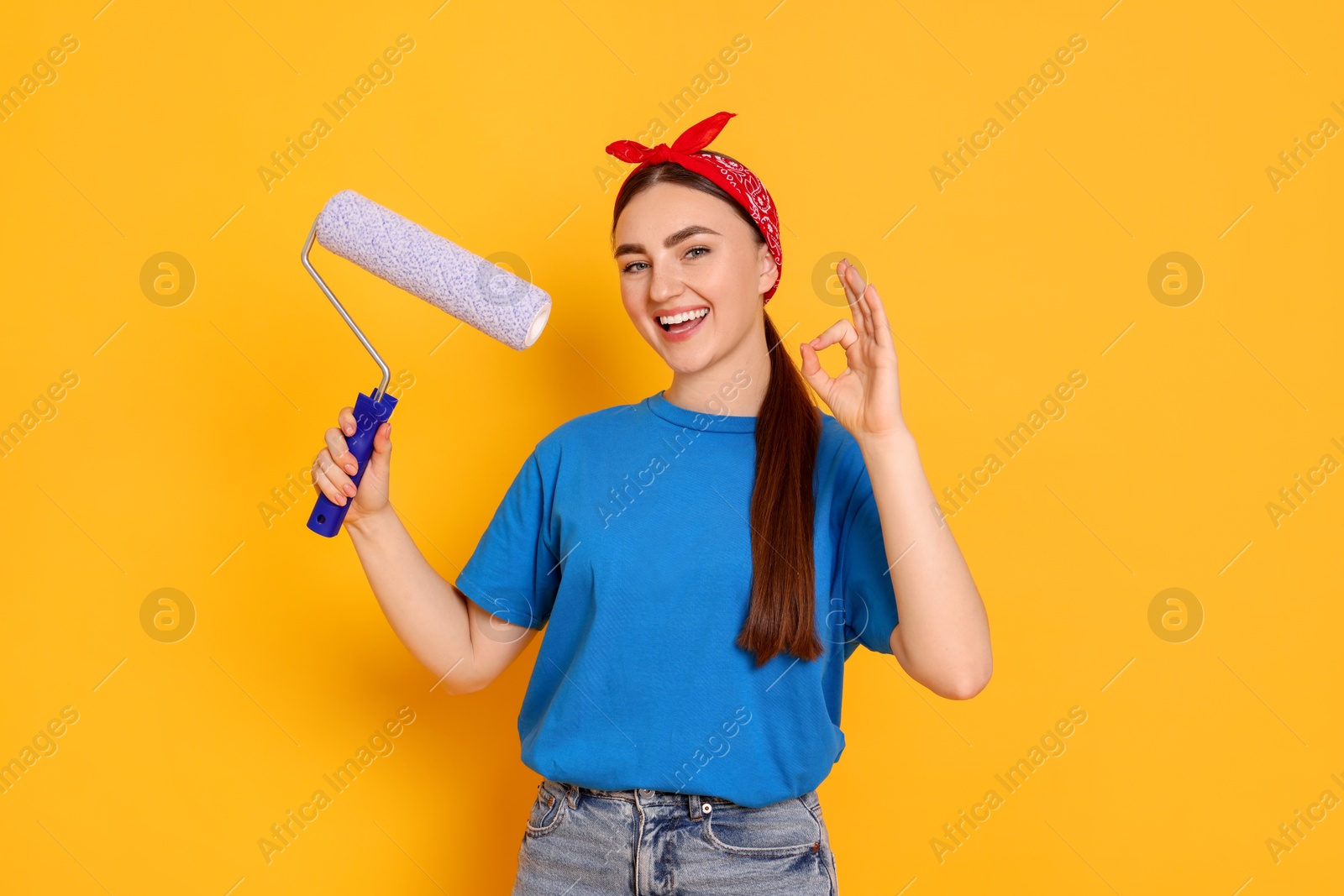 Photo of Portrait of young decorator with paint roller showing ok gesture on orange background