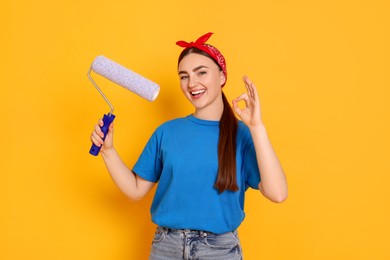 Photo of Portrait of young decorator with paint roller showing ok gesture on orange background