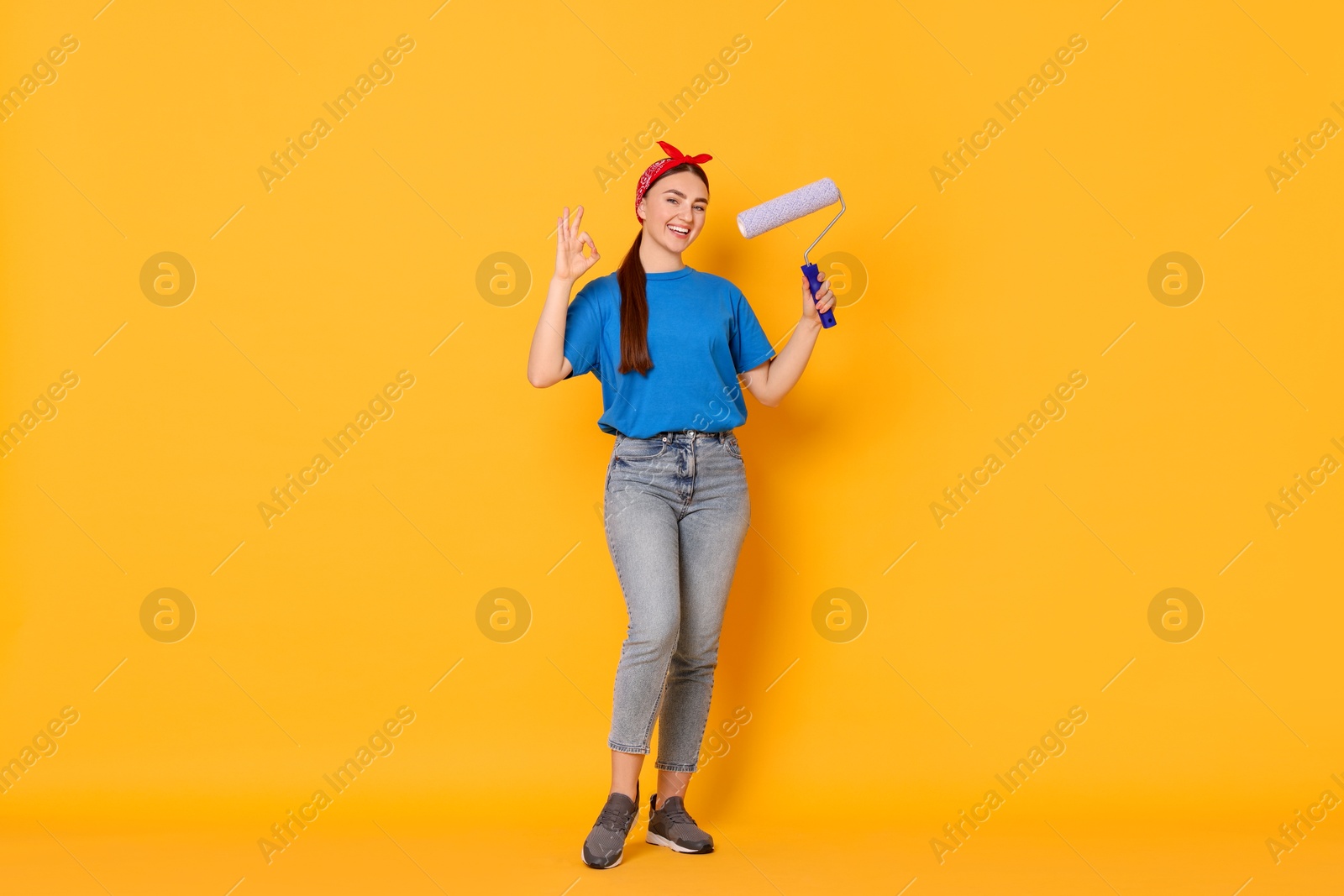 Photo of Portrait of young decorator with paint roller showing ok gesture on orange background