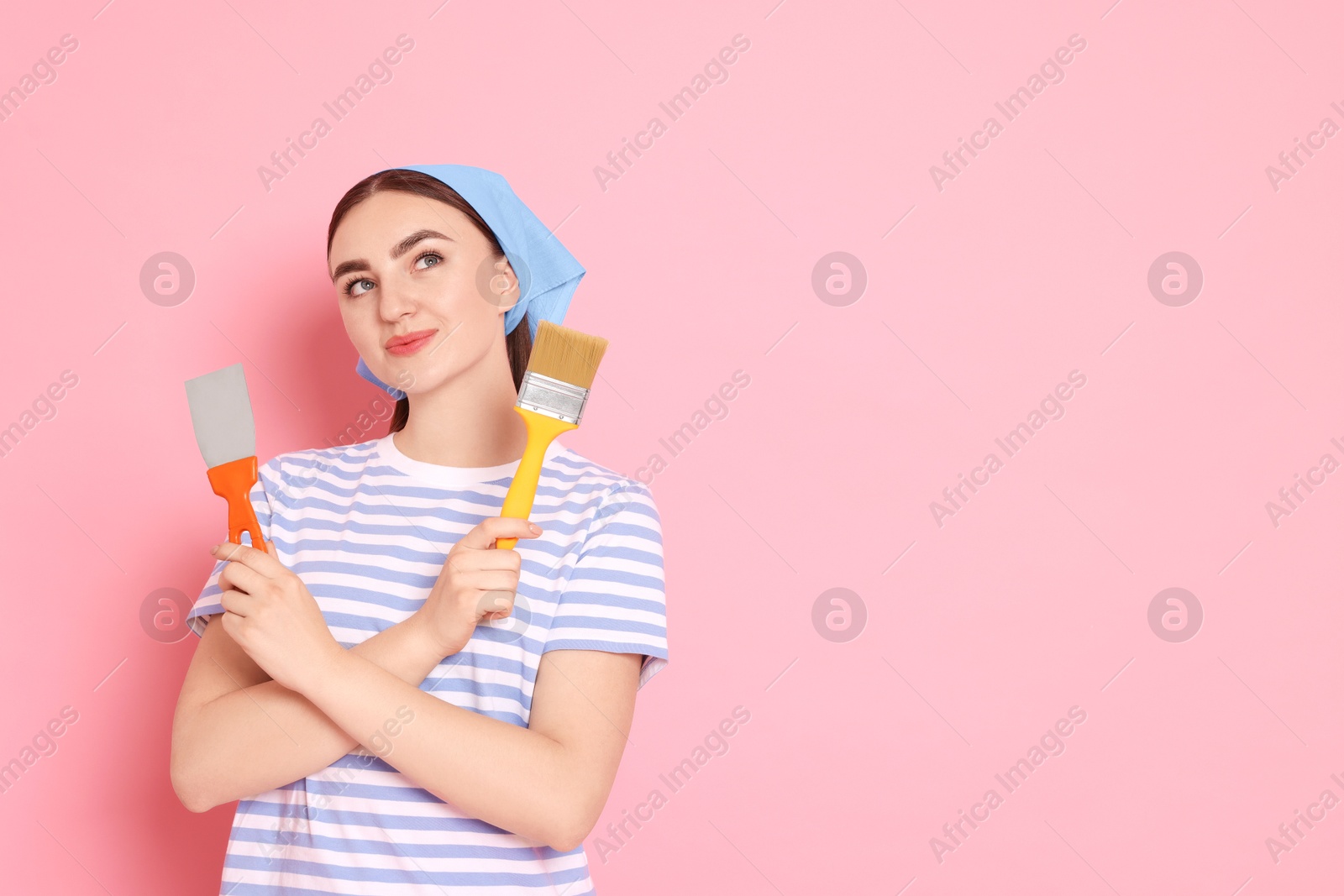 Photo of Portrait of young decorator with putty knife and brush on pink background, space for text