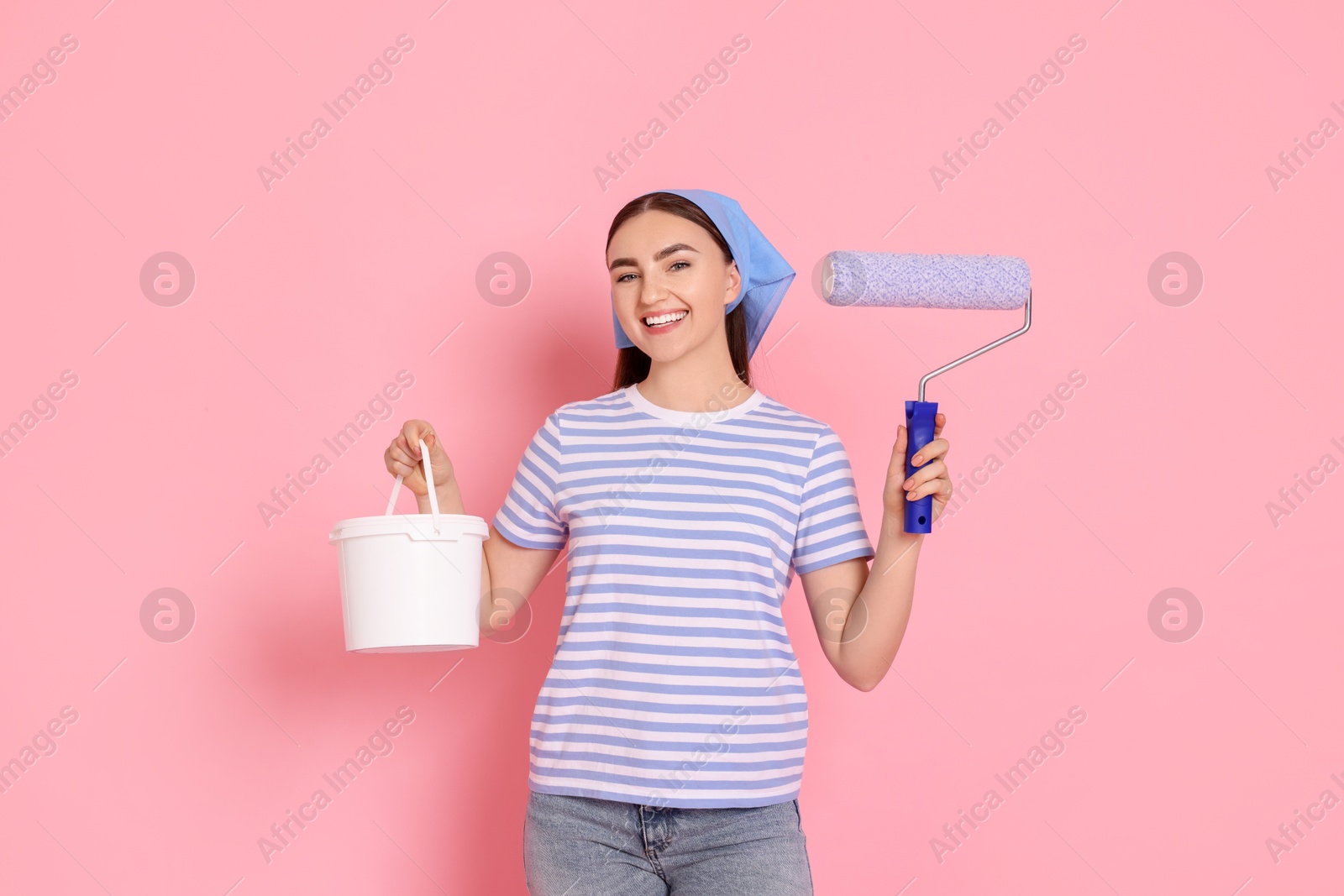 Photo of Portrait of young decorator with paint roller and bucket on pink background