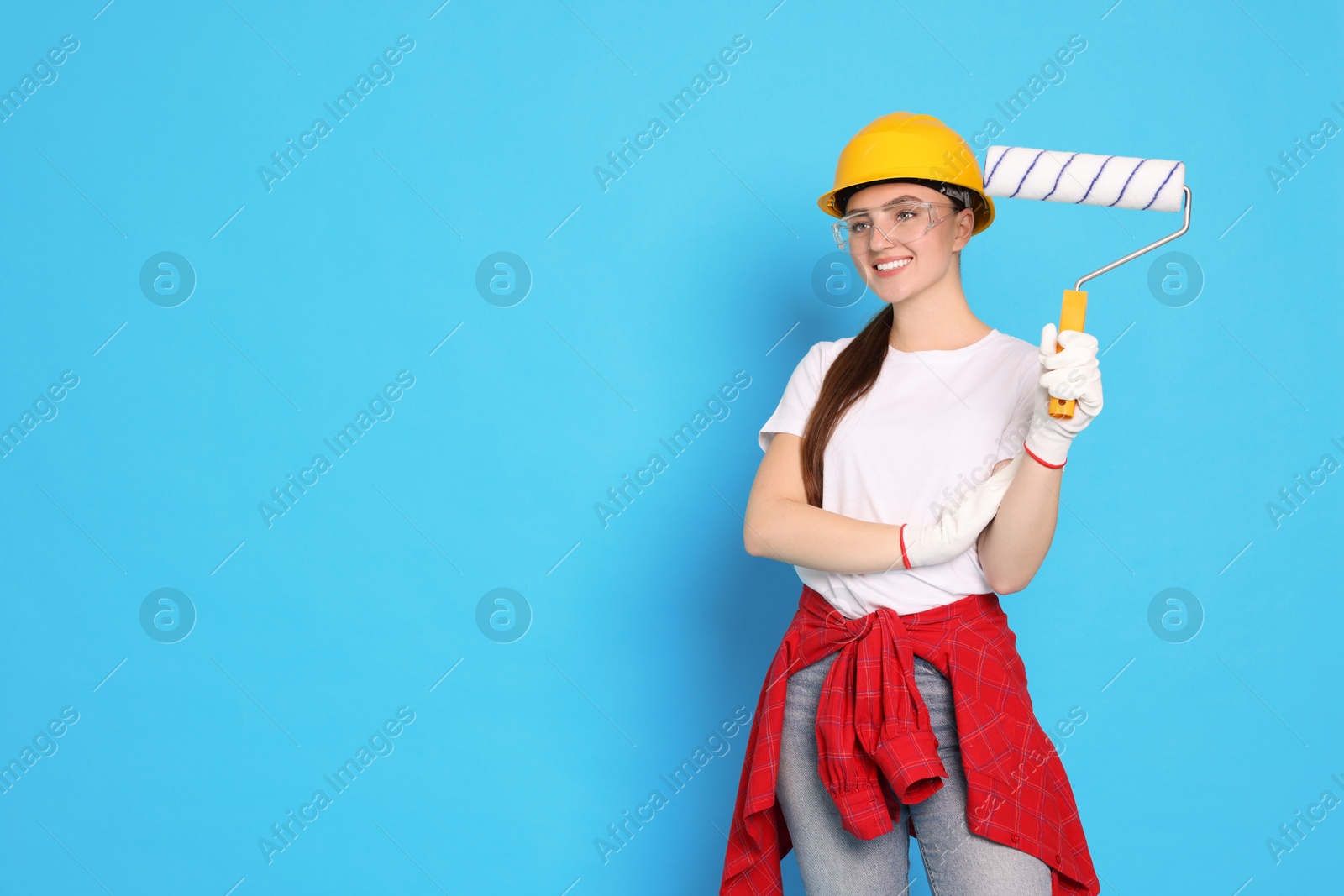 Photo of Portrait of young decorator with paint roller on light blue background, space for text