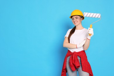 Photo of Portrait of young decorator with paint roller on light blue background, space for text