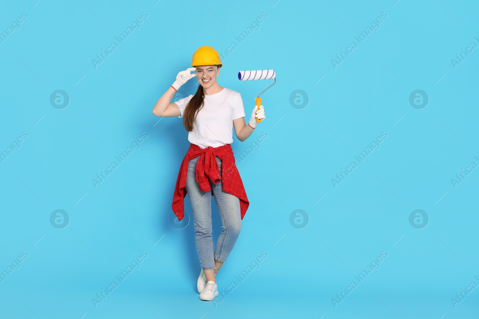 Photo of Young decorator with paint roller on light blue background