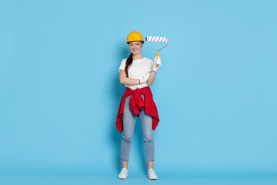 Photo of Young decorator with paint roller on light blue background