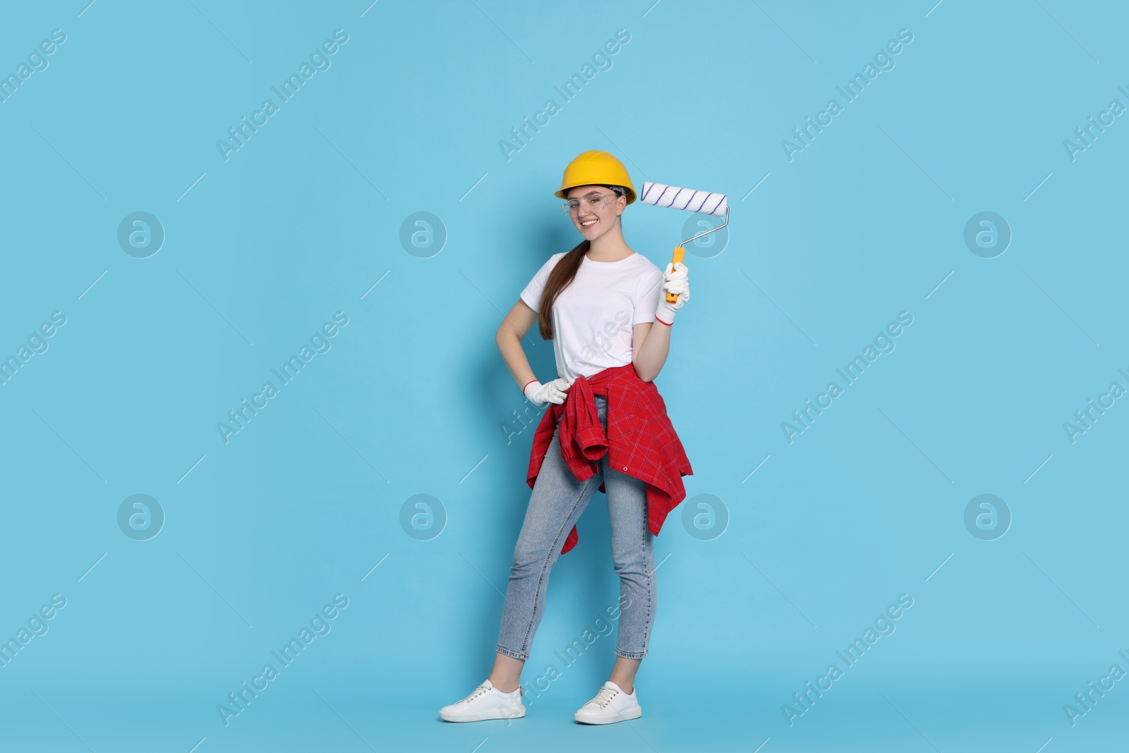 Photo of Young decorator with paint roller on light blue background