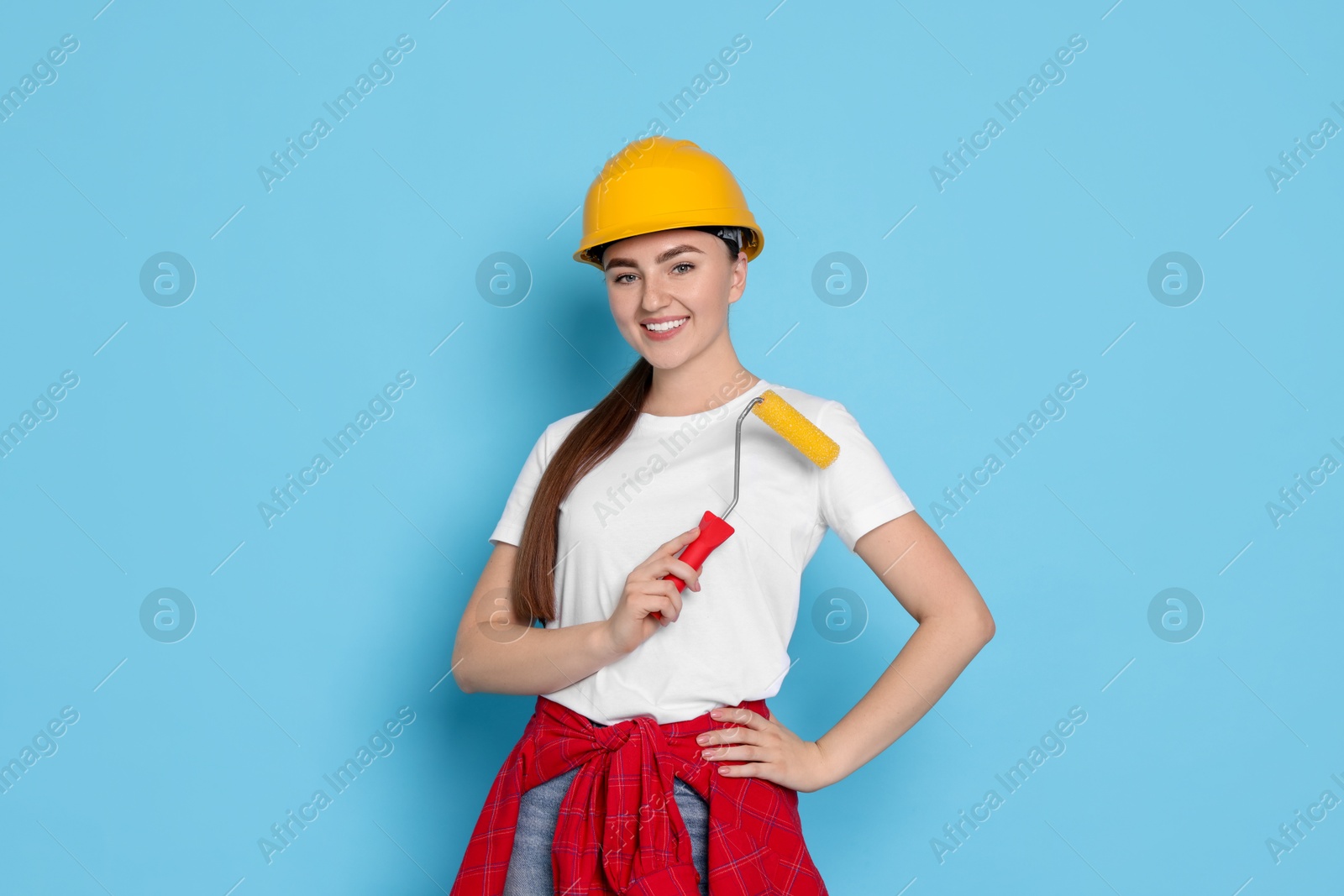 Photo of Portrait of young decorator with paint roller on light blue background