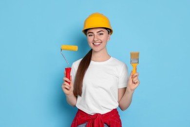 Photo of Portrait of young decorator with paint roller and brush on light blue background