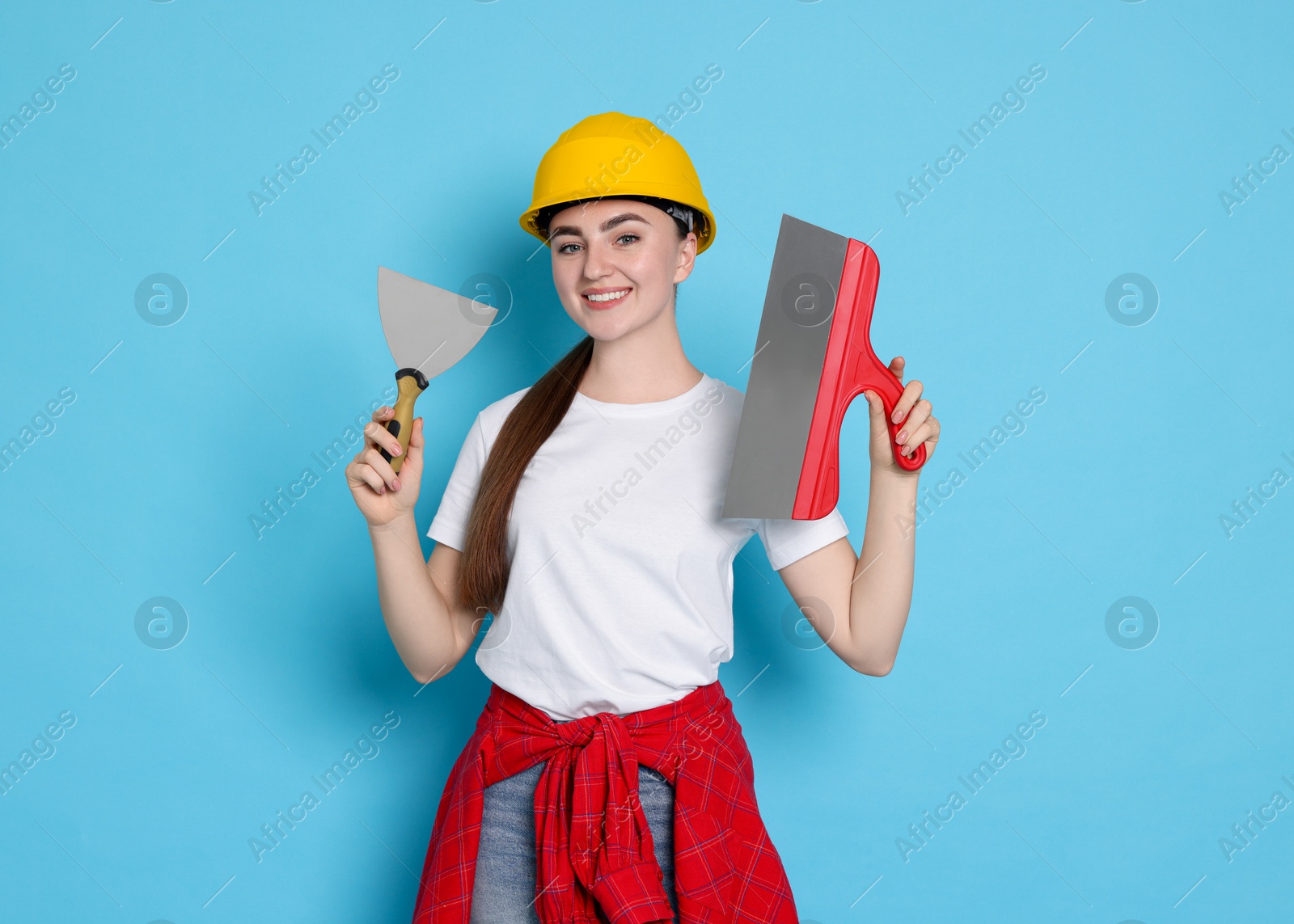 Photo of Portrait of young decorator with putty knives on light blue background