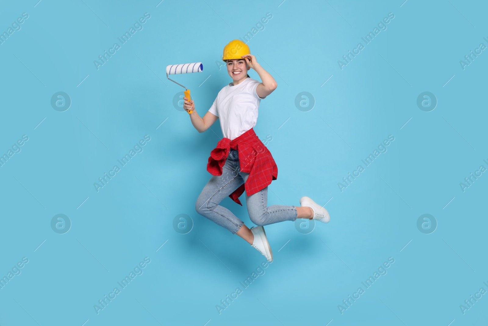 Photo of Young decorator with paint roller jumping on light blue background