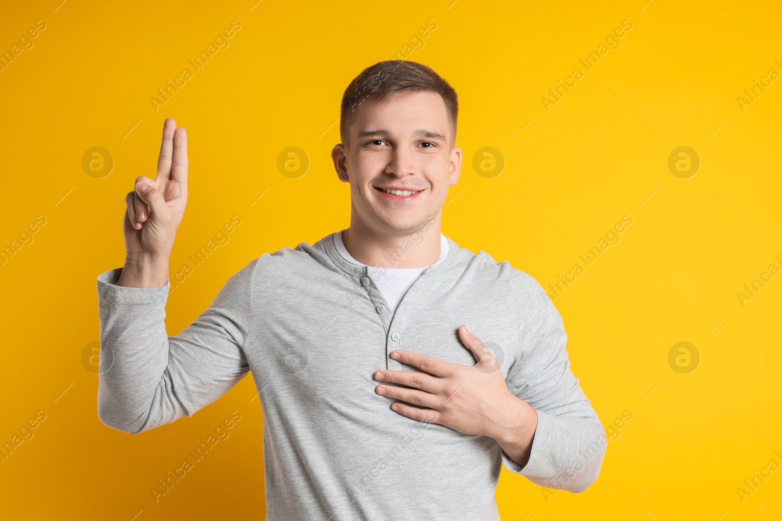 Photo of Man showing oath gesture on orange background. Making promise