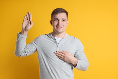 Photo of Man making promise with raised hand on orange background. Oath gesture