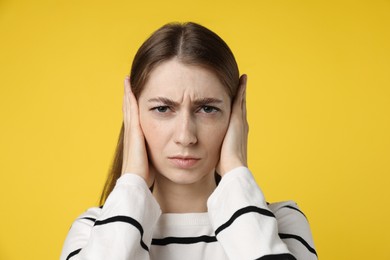 Photo of Woman covering her ears on dark yellow background