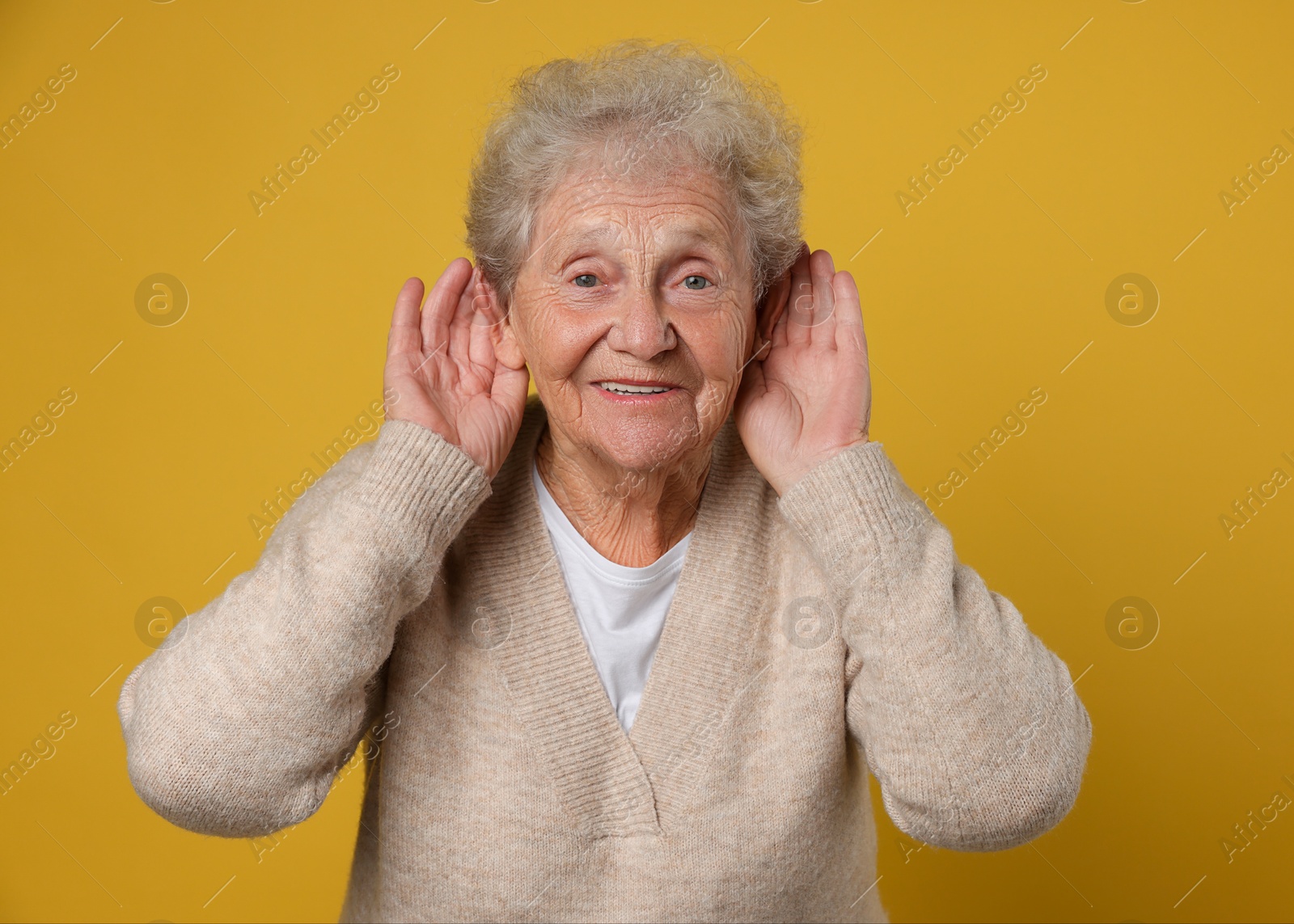 Photo of Senior woman showing hand to ear gesture on dark yellow background