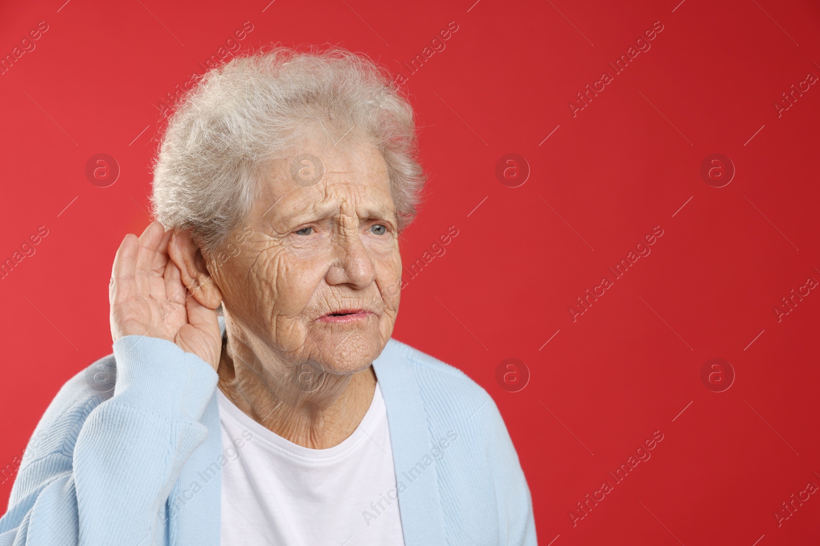 Photo of Senior woman showing hand to ear gesture on red background, space for text