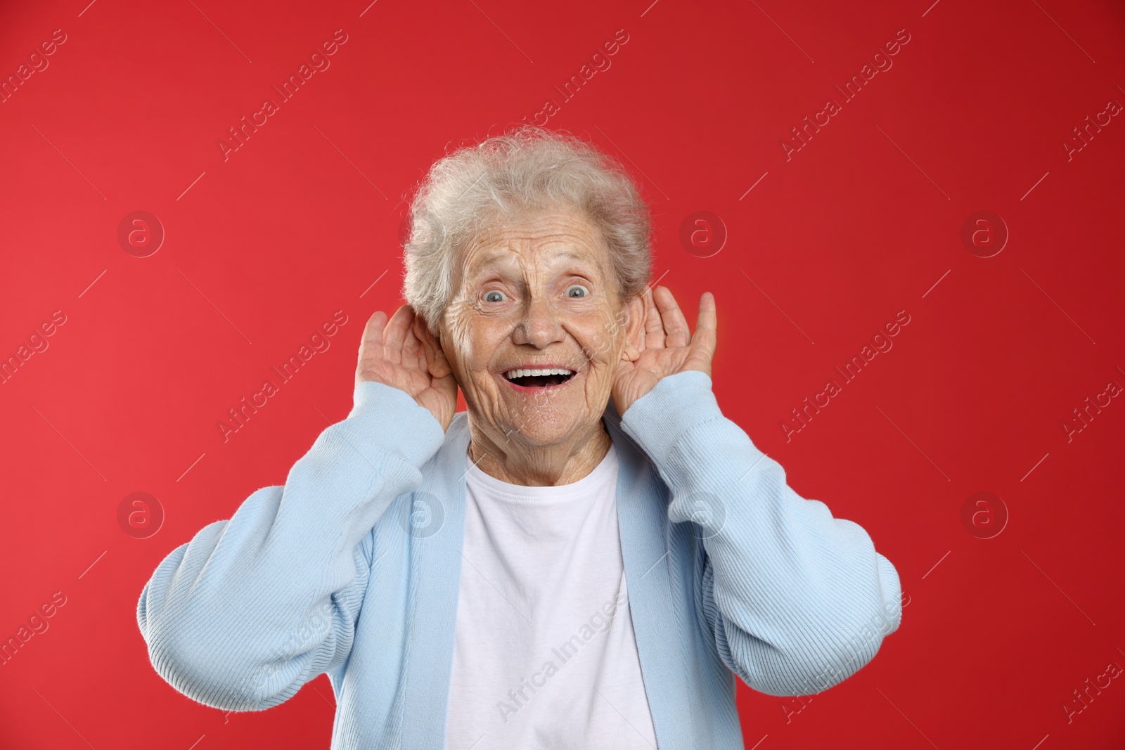 Photo of Senior woman showing hand to ear gesture on red background