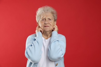 Photo of Senior woman covering her ears with fingers on red background