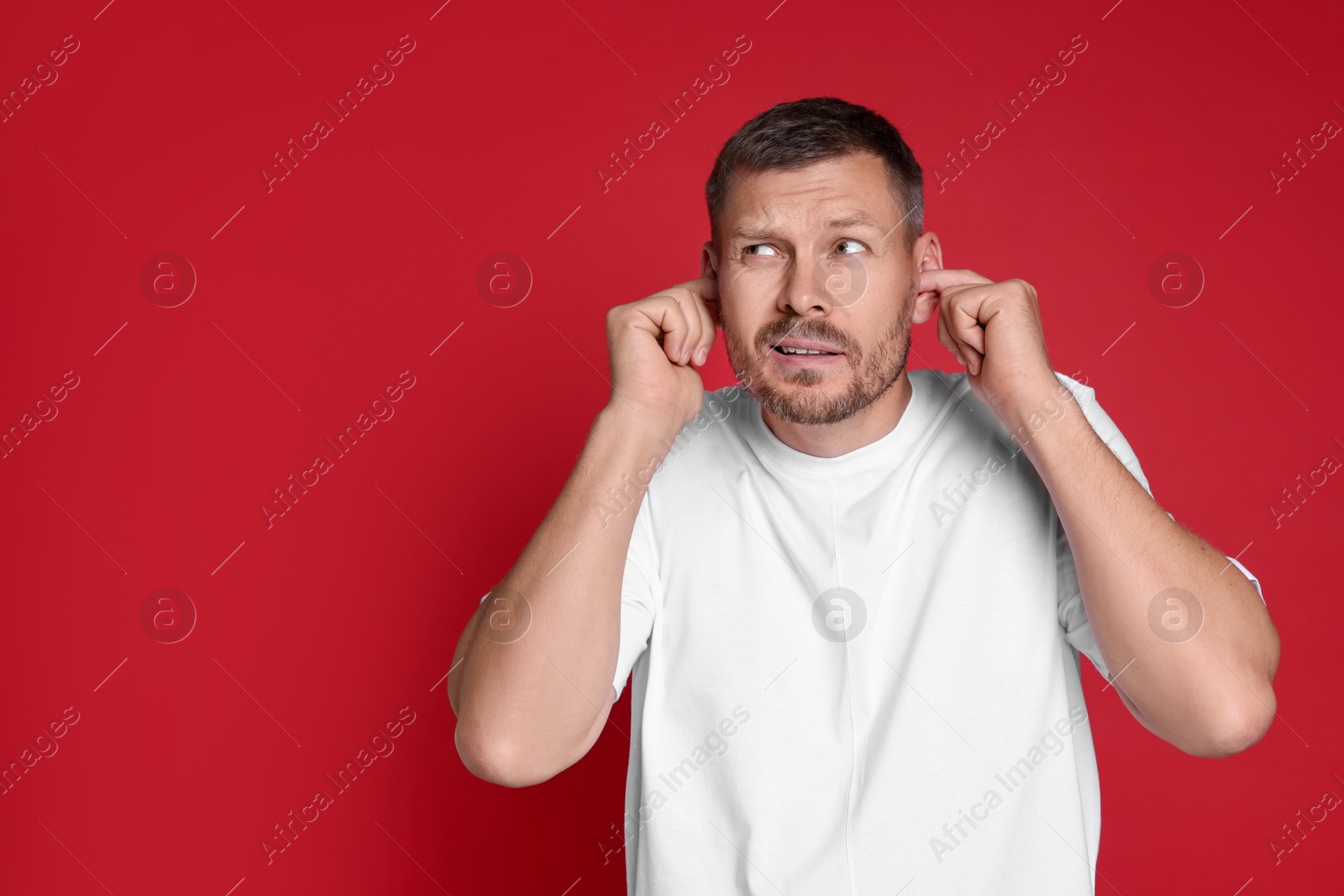 Photo of Man covering his ears with fingers on red background, space for text