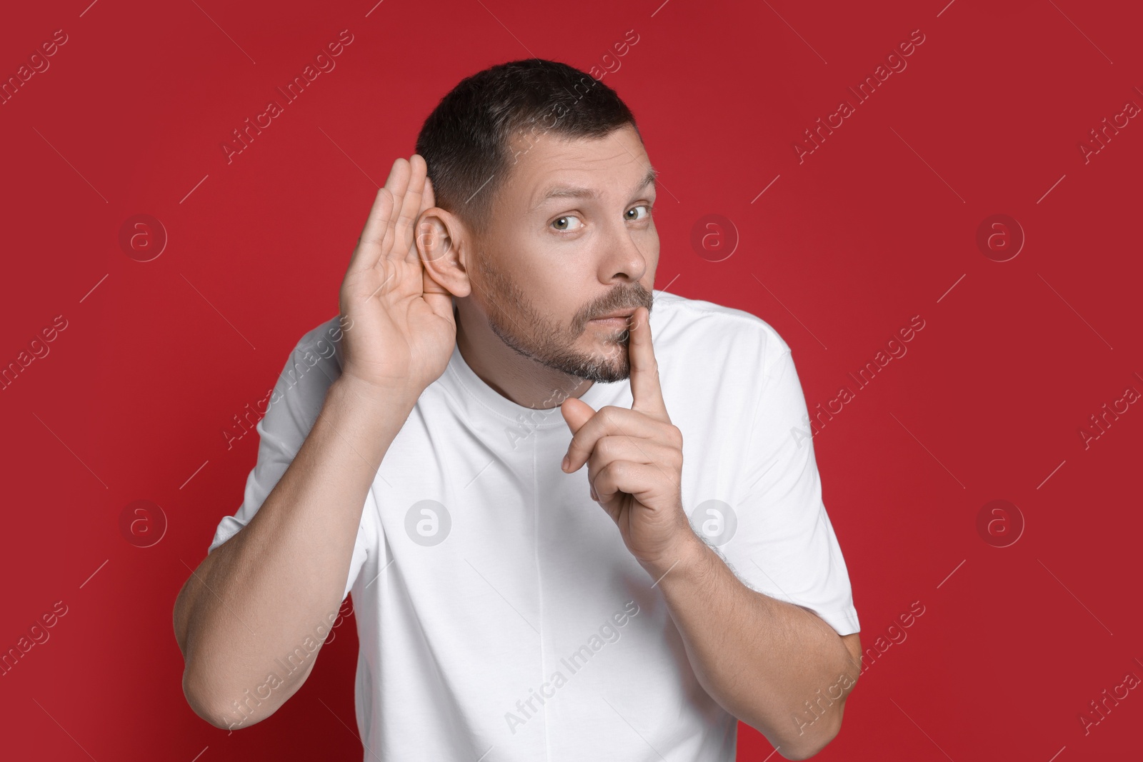 Photo of Man showing hand to ear gesture on red background