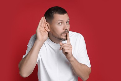 Photo of Man showing hand to ear gesture on red background