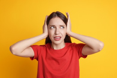 Woman covering her ears on orange background