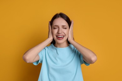 Photo of Woman covering her ears on orange background