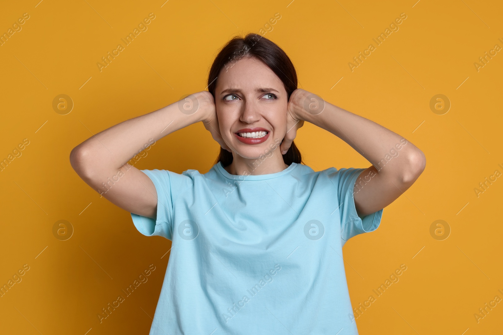 Photo of Woman covering her ears on orange background