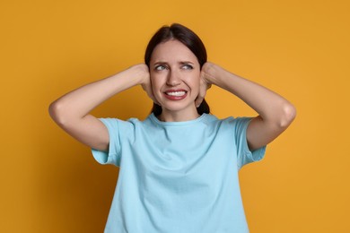 Woman covering her ears on orange background