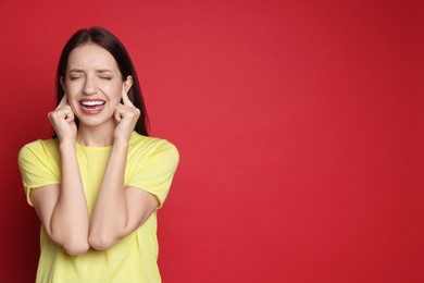 Photo of Woman covering her ears with fingers on red background, space for text