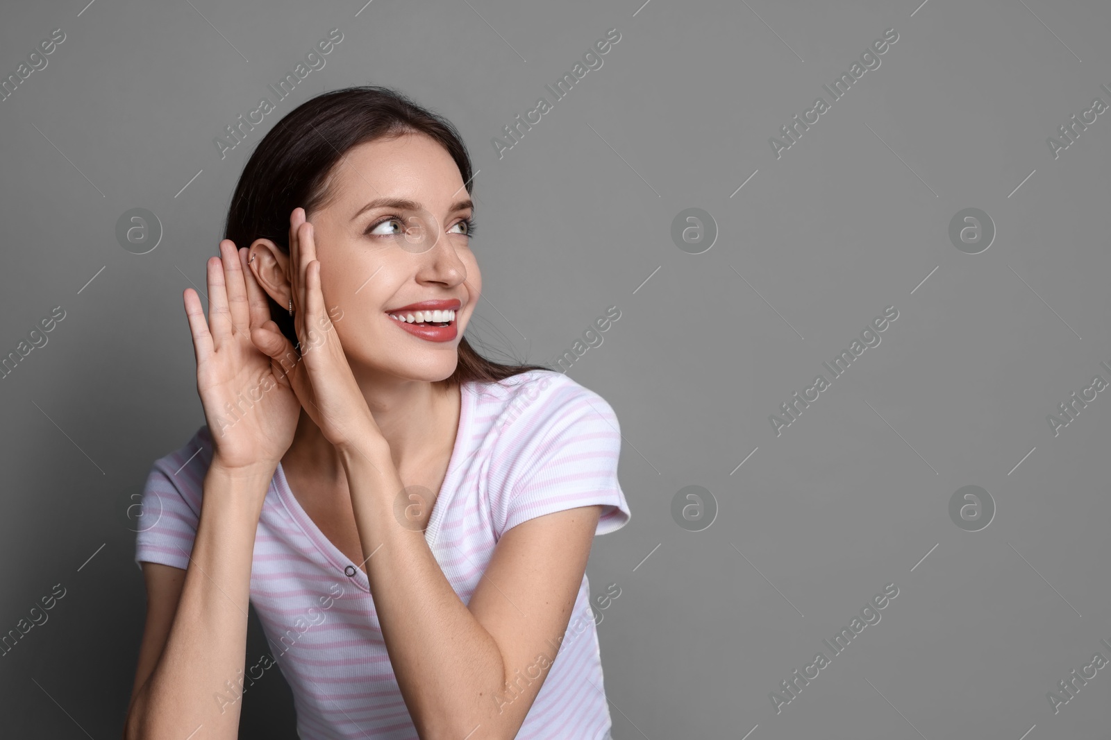 Photo of Woman showing hand to ear gesture on grey background, space for text