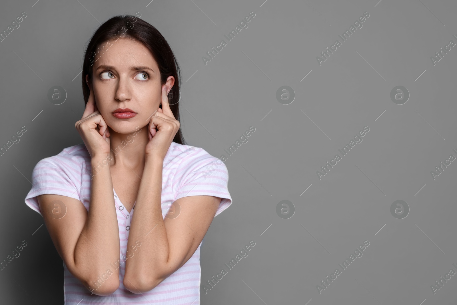 Photo of Woman covering her ears with fingers on grey background, space for text