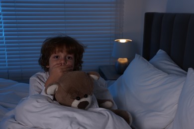 Photo of Scared boy with teddy bear in bed at night