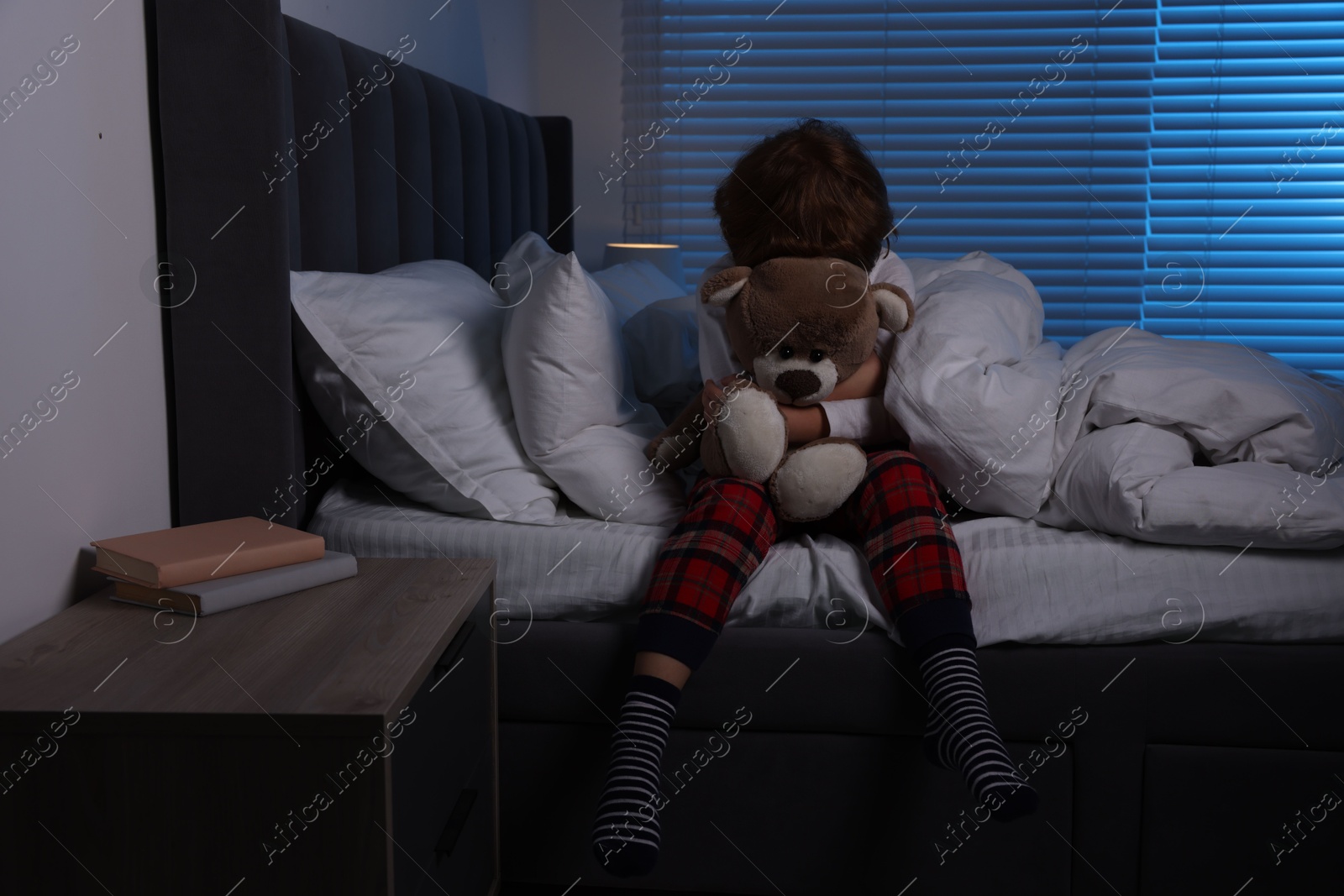 Photo of Scared boy with teddy bear on bed at night