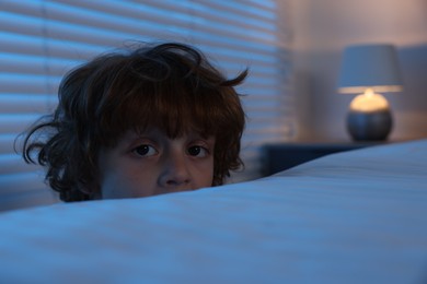 Photo of Scared boy hiding behind bed at night. Space for text