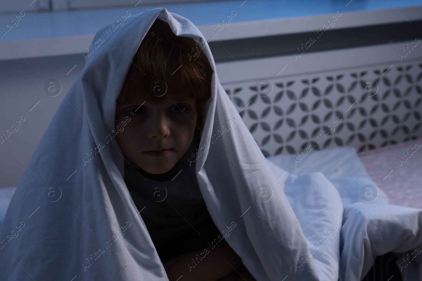 Photo of Afraid boy under blanket on bed at night