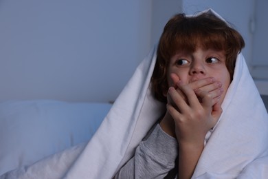 Photo of Afraid boy under blanket on bed at night. Space for text