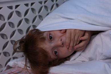 Photo of Afraid boy under blanket on bed at night