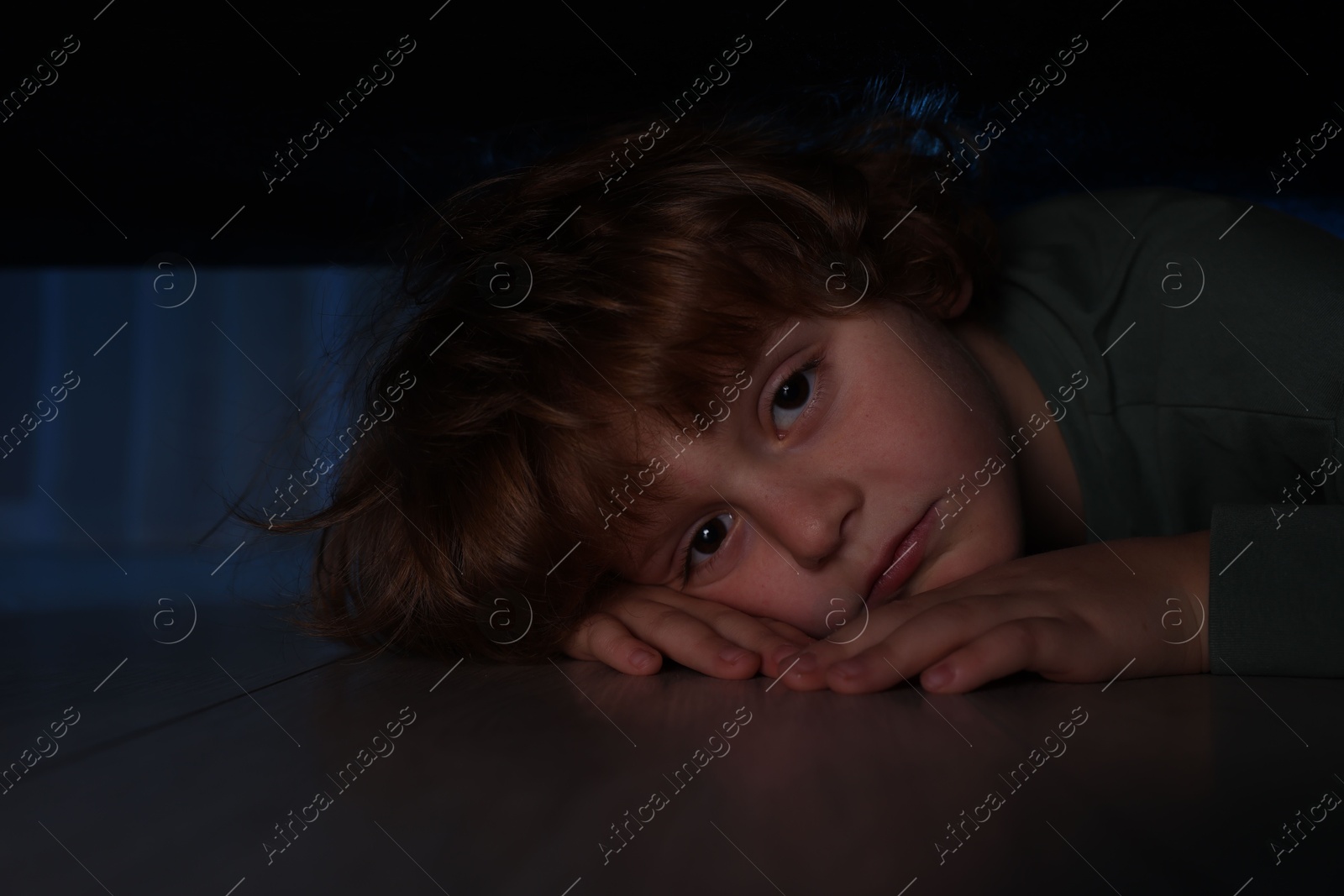 Photo of Fearful boy hiding under bed at night