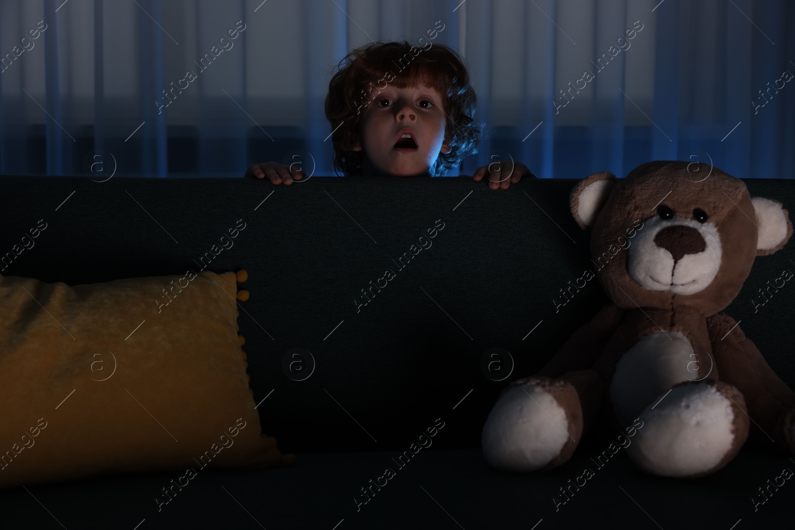 Photo of Fearful boy hiding behind sofa at night