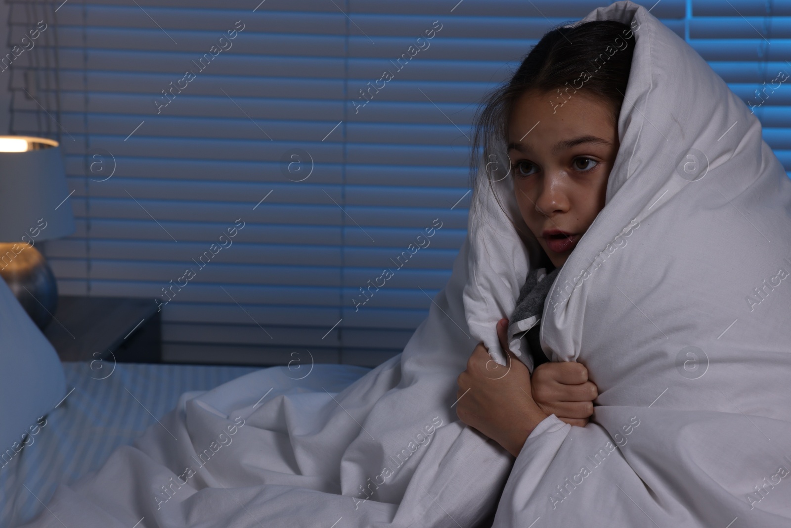 Photo of Afraid girl wrapped in duvet on bed at night. Space for text