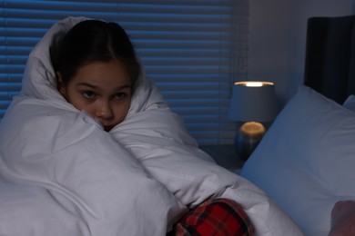 Photo of Afraid girl wrapped in duvet on bed at night