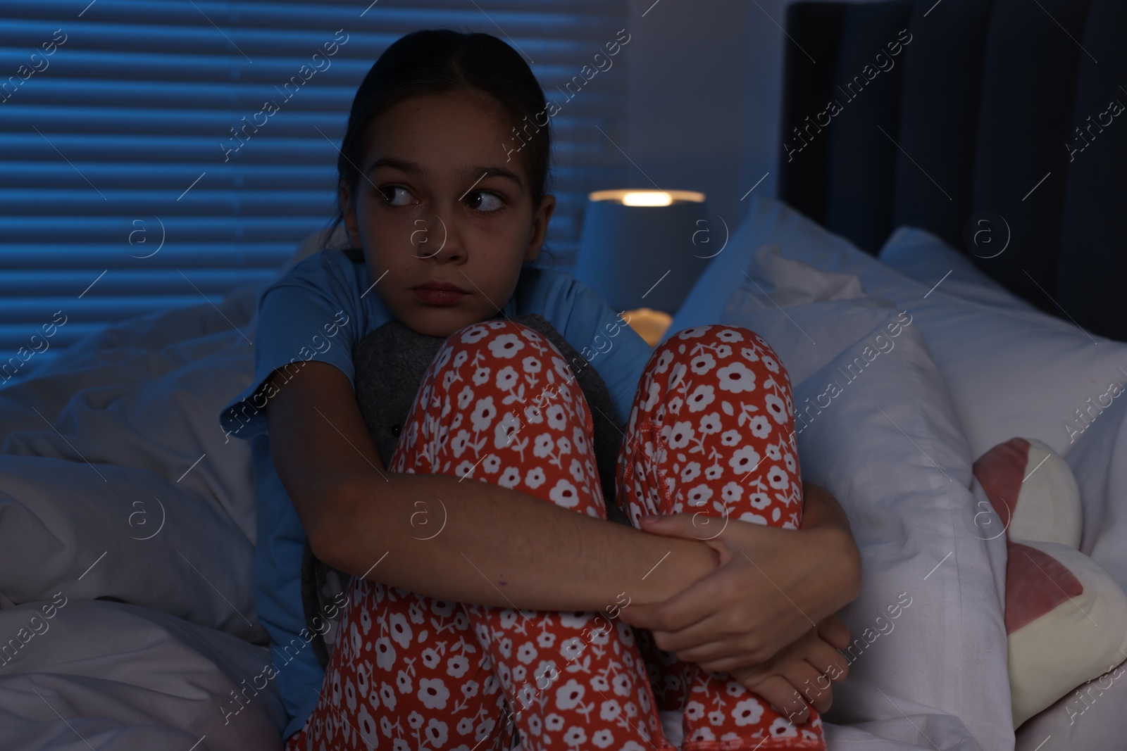 Photo of Fearful girl sitting on bed at night